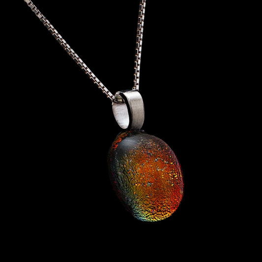 Handmade round dichroic glass pendant necklace showing colour-shifting red, gold, and green tones