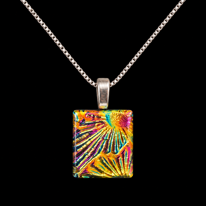 A silver chain necklace with a square pendant featuring a vibrant, multicolored abstract pattern of radiating lines in yellow, orange, pink, and blue, set against a solid black background.