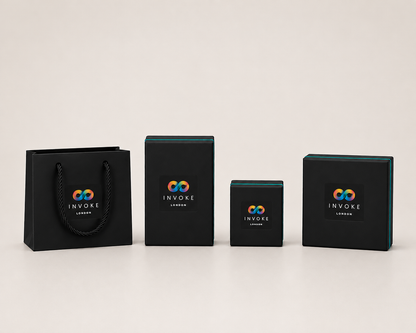 A set of black branded packaging accessories from Invoke London, including a shopping bag and three different sized rectangular boxes, arranged on a white reflective surface.