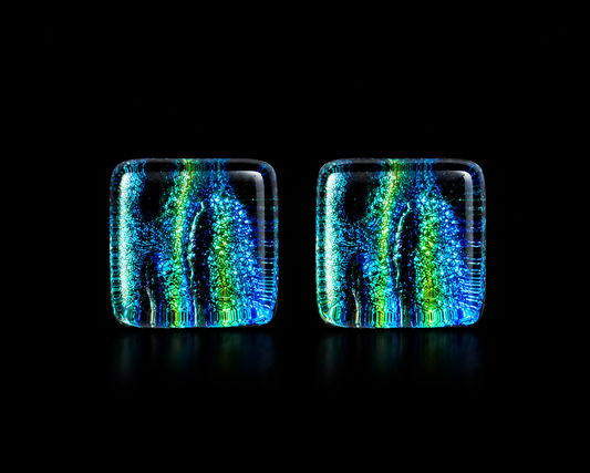 A pair of cube glass tiles with rounded corners, featuring vibrant vertical patterns of blue, green, and yellow on a black background.