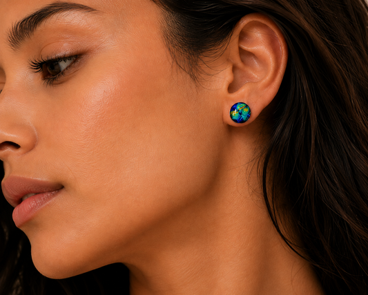 Close-up of a woman's ear wearing a small round stud earring with a colorful globe design in blue, green, and yellow tones.