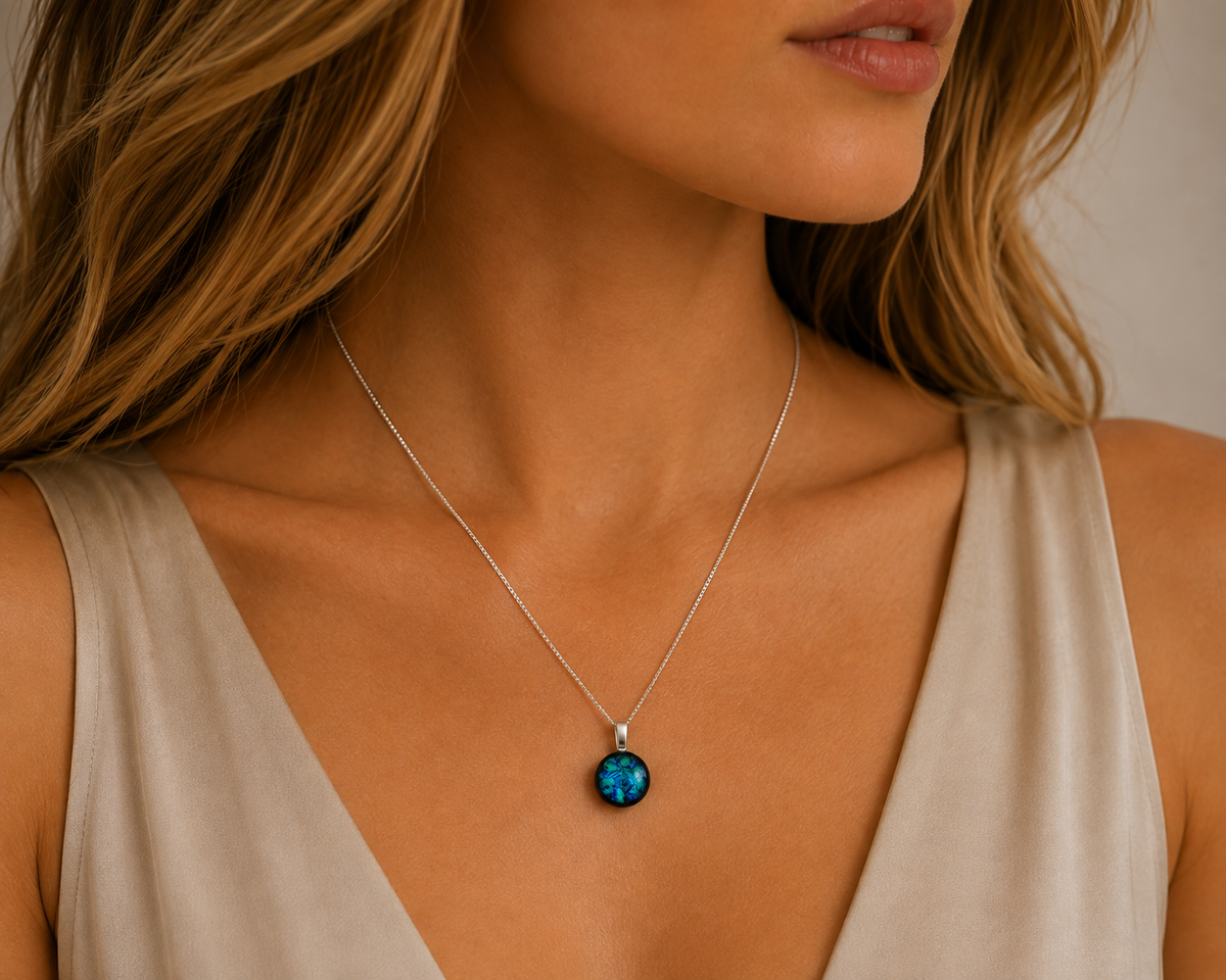 A close-up of a woman wearing a delicate silver chain necklace with a round, dark blue-green stone pendant, paired with a beige sleeveless top.