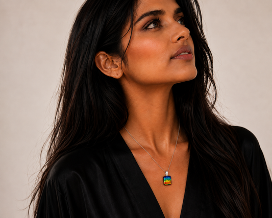 A woman with long dark hair wearing a silver chain necklace with a square pendant featuring the colorful Indian flag, set against a plain beige background.