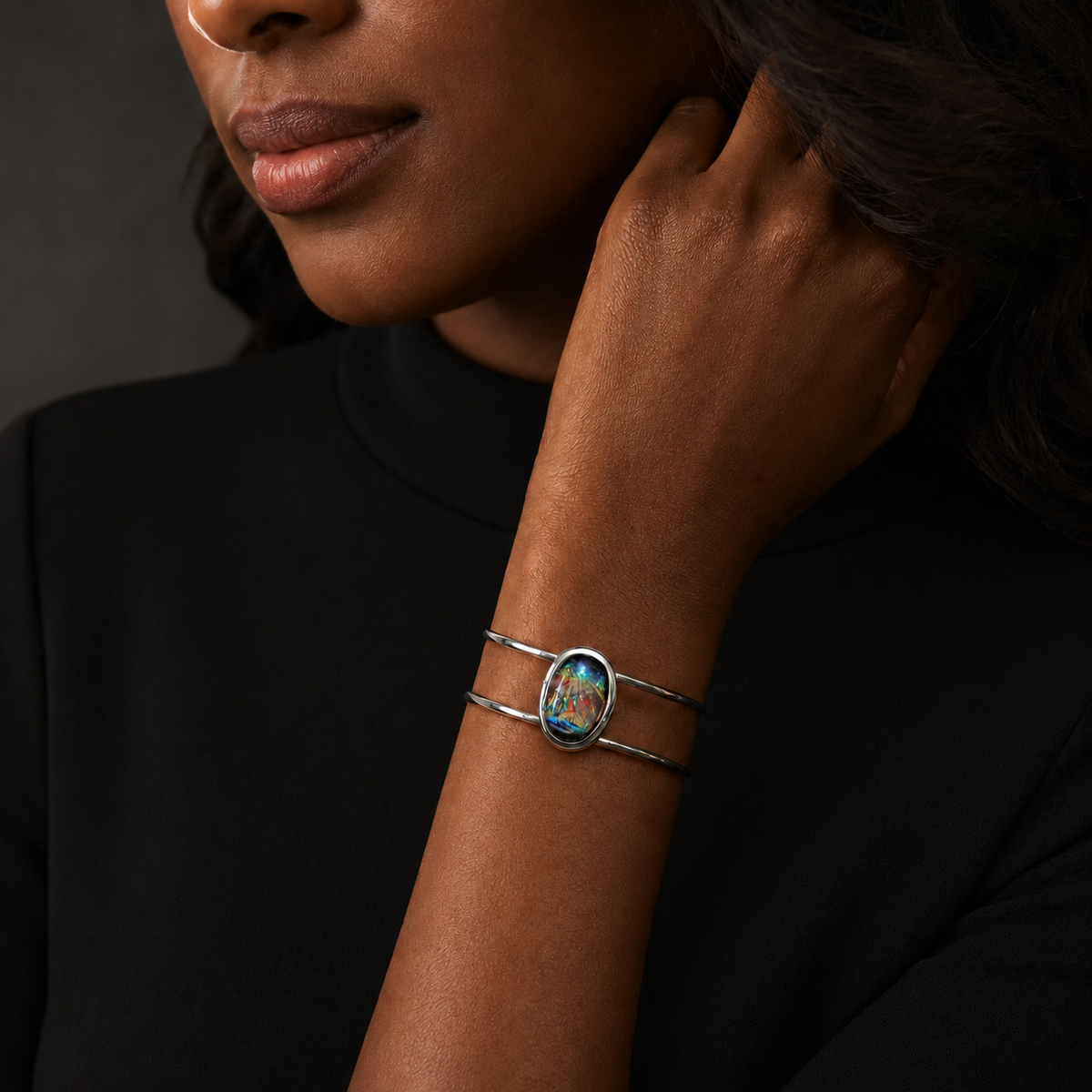 A close-up of a model wearing a silver wrap bracelet with a colorful oval centerpiece featuring a floral design.