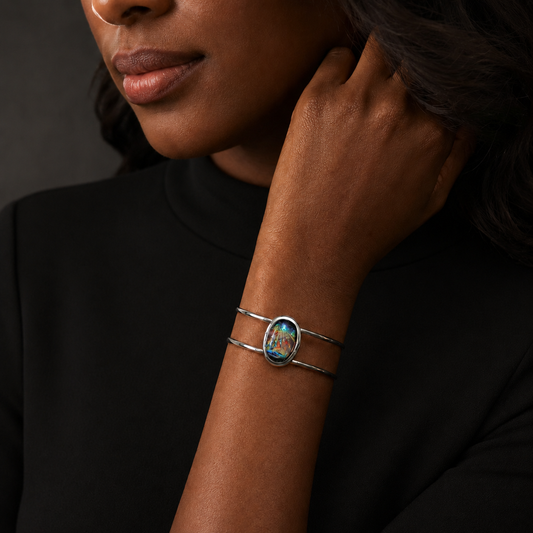 A close-up of a model wearing a silver wrap bracelet with a colorful oval centerpiece featuring a floral design.