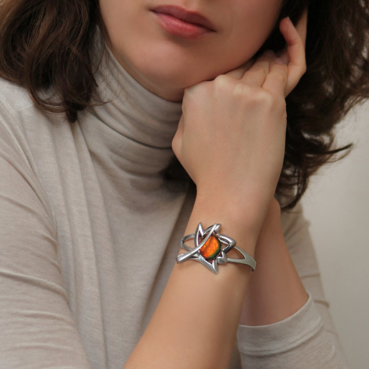 Woman wearing a silver bracelet with an orange dichroic stone on a neutral background