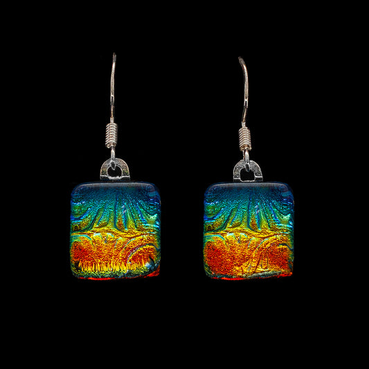 A pair of colorful, square-shaped, dichroic glass drop earrings with a geometric pattern, showcasing a range of colors including blue, green, and orange.