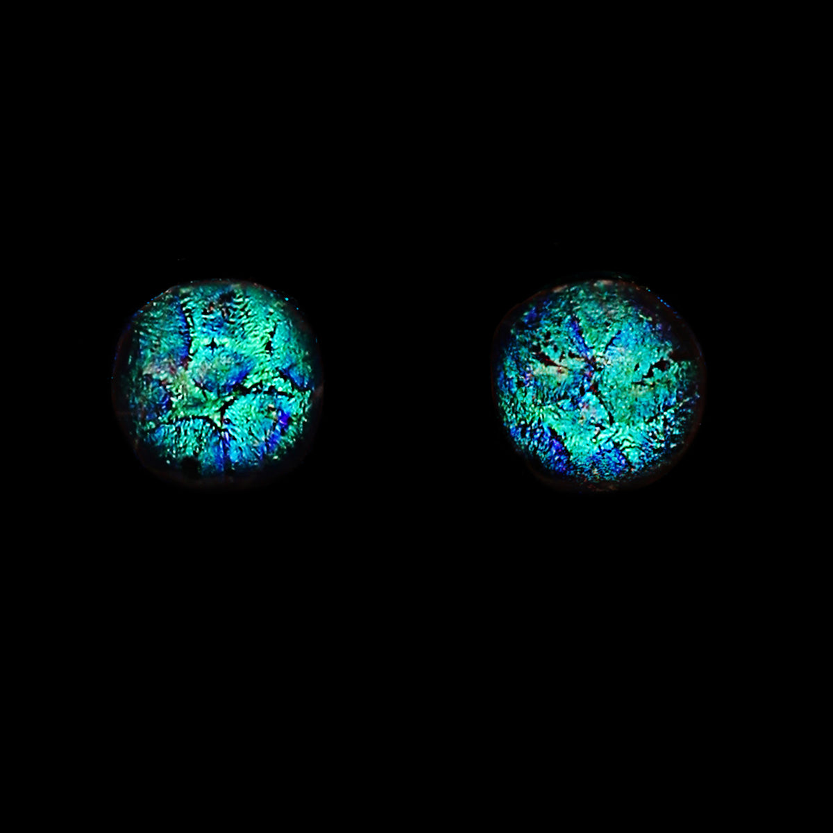 Two round cabochon gemstones with vibrant blue, green, and purple iridescent opal patterns, displayed side-by-side on a solid black background.