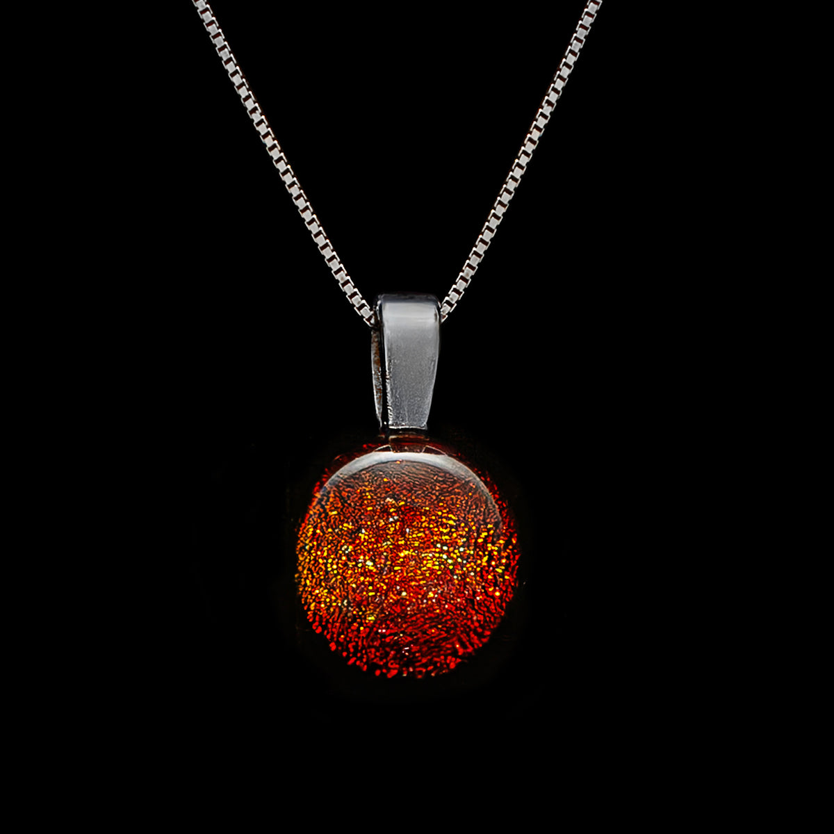 A round orange dichroic glass pendant necklace with a silver chain, displayed against a black background.