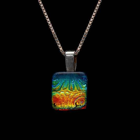 A colorful, geometric pendant necklace with a cube shape and a Dichroic glass cap, displayed against a black background.
