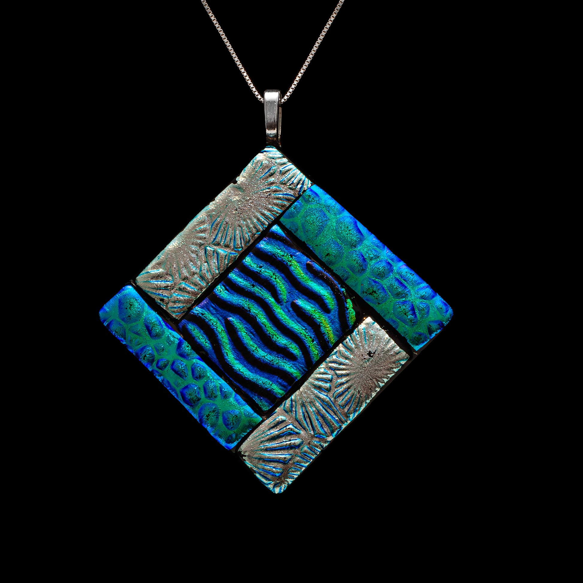 Close-up of a green fused glass diamond-shaped pendant with embossed silver segments and a central wavy dichroic glass design, inspired by the sea, from the Ocean Collection by Invoke London.